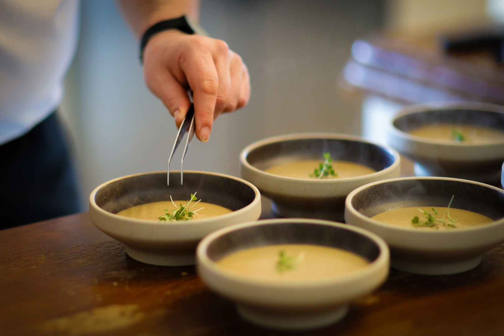 Chef hands garnishing steaming soup bowls with tweezers during a cooking class